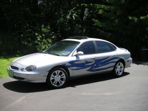 1999 Ford Taurus - A silver sedan with custom blue flame decals is shown from a three-quarter front angle.