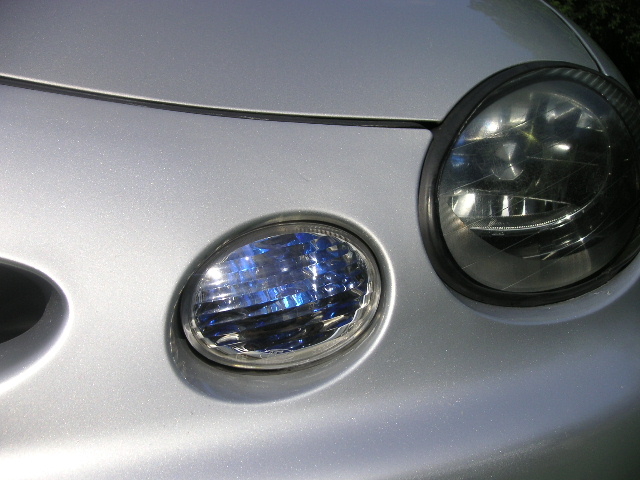 Silver car front corner with headlights and fog light. Watermark reads SUPERMOTORS.NET