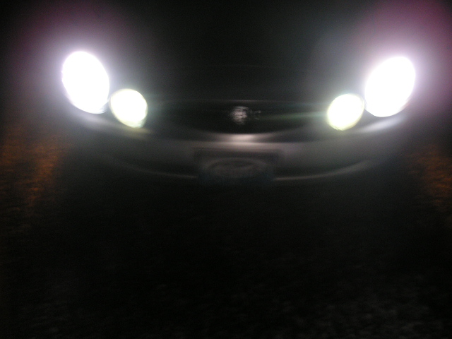 Car headlights illuminated at night, showing the front grille and emblem