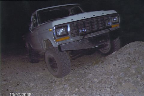 1990 Ford Bronco - white lifted Ford pickup with chrome grille and large off-road tires photographed front-on at night on rocky ground.