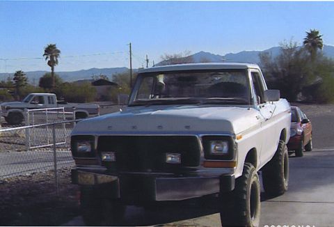 1990 Ford Bronco - white lifted Ford pickup with black grille parked in a residential yard with palm trees and mountains in the distance.