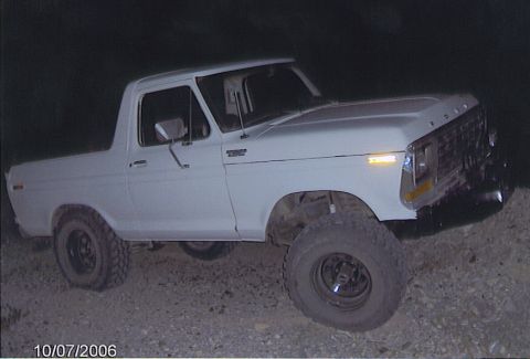 1990 Ford Bronco - white lifted Ford pickup with Ford-stamped tailgate and large tires shown in side profile at night on rocky terrain.