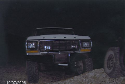 1990 Ford Bronco - Front view of a white lifted Ford truck at night, headlights and amber turn signals reflecting against a dark background.