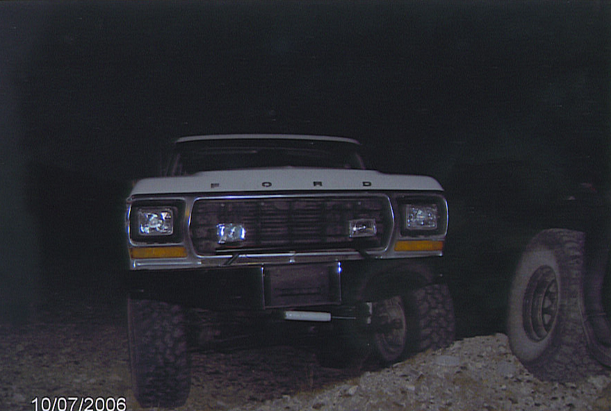Front of a white lifted Ford truck at night with headlights and grille visible