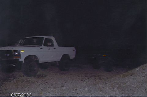 1990 Ford Bronco - white lifted Ford truck parked on a graded dirt slope at dusk, with a second dark vehicle barely visible alongside.