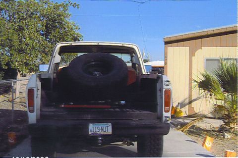 1990 Ford Bronco - Rear view of a white lifted truck with a spare tire mounted in the bed and an Arizona license plate, parked by a building.