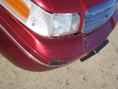 1991 Ford LTD Crown Victoria - The front corner of a red sedan shows scuffs on the bumper and a chrome grille.