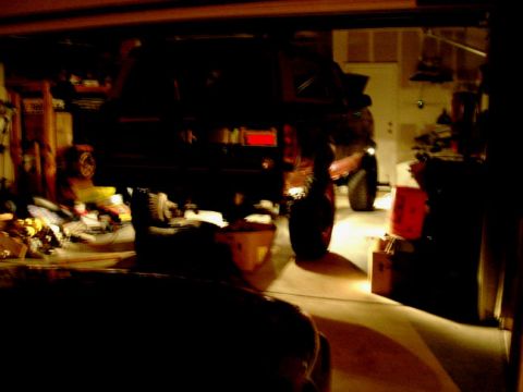 1994 Ford Bronco - An SUV is raised on a jack in a dimly lit garage, with various items visible in the background.