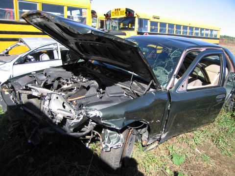 1991 Ford LTD Crown Victoria - Damaged dark green sedan with its hood open, parked next to another vehicle and school buses.