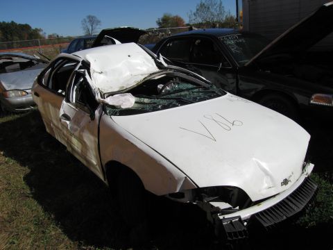 1991 Ford LTD Crown Victoria - A severely damaged white sedan sits in a junkyard, with other vehicles visible in the background.