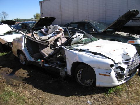 1991 Ford LTD Crown Victoria - Junkyard scene with a severely damaged white sedan in the foreground and other vehicles behind it.