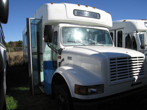 1991 Ford LTD Crown Victoria - A white bus with its door open is parked next to another bus under a clear blue sky.