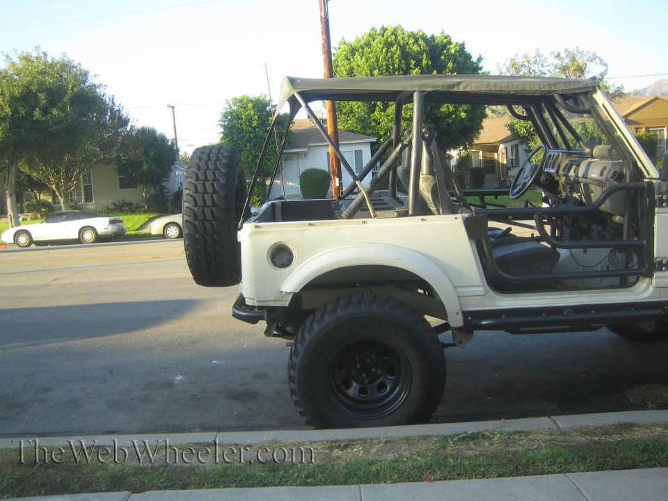 1987 Suzuki Samurai with roll cage and spare tire mounted on the back, parked on a street