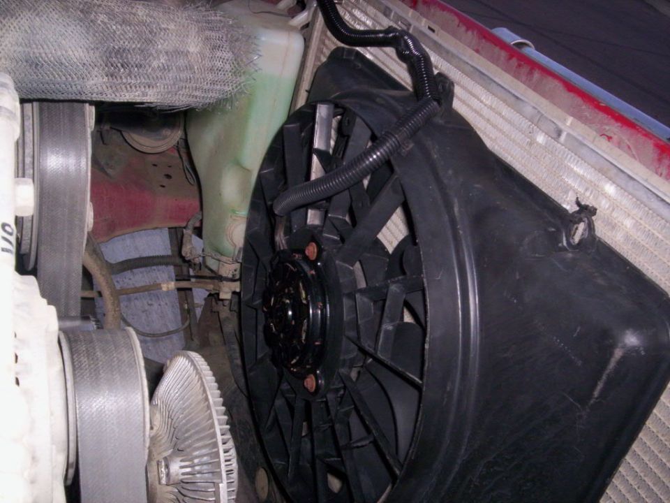 Engine bay view of a black electric cooling fan and radiator with a green fluid reservoir