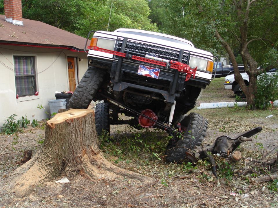 White lifted Ford 4x4 flexed on a tree stump showing red differential and radius arms
