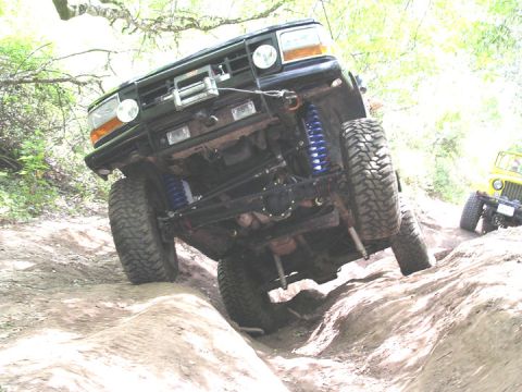 1994 Ford Bronco - A black 1994 Ford Bronco navigates a rocky off-road trail, its lifted suspension and aggressive tires.