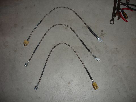 1996 Ford Bronco - Three braided steel cables, likely brake lines or similar, are laid out on a concrete surface with various connectors.