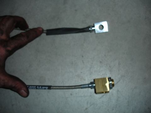 1996 Ford Bronco - Braided brake line and a metal bracket are held against a concrete surface.