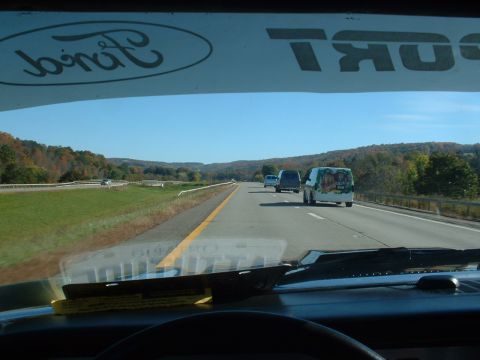 1978 Ford Mustang II - Multiple vans travel down a highway on a clear day, with a Ford logo visible on the interior windshield.