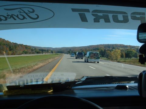 1978 Ford Mustang II - Multiple vans travel down a highway on a clear day, with wooded hills visible on either side.