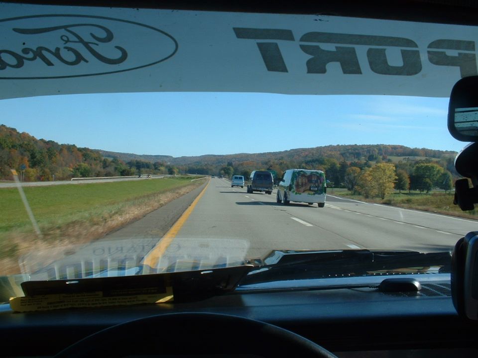 View from inside a vehicle looking at several vans driving on a highway with rolling hills in the background