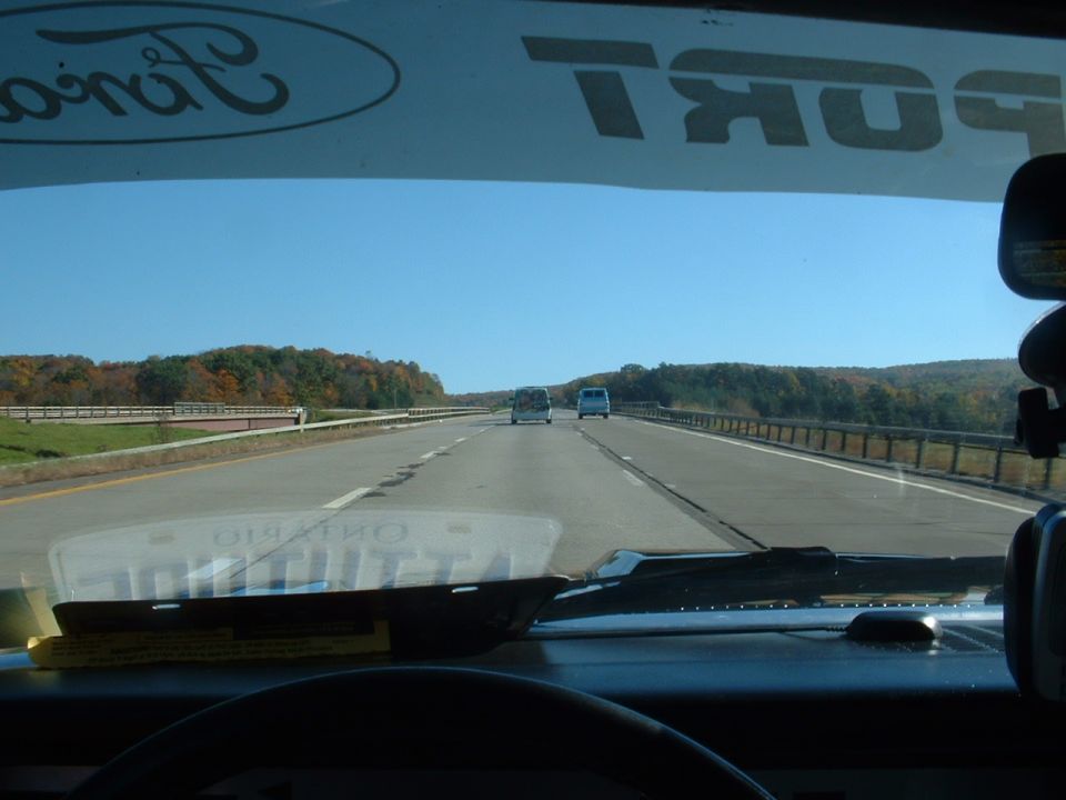 View from inside a vehicle driving on a highway, with two vans ahead and trees lining the road