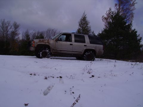 2000 Chevrolet Tahoe - SUV with snow chains on tires driving through a snowy landscape.