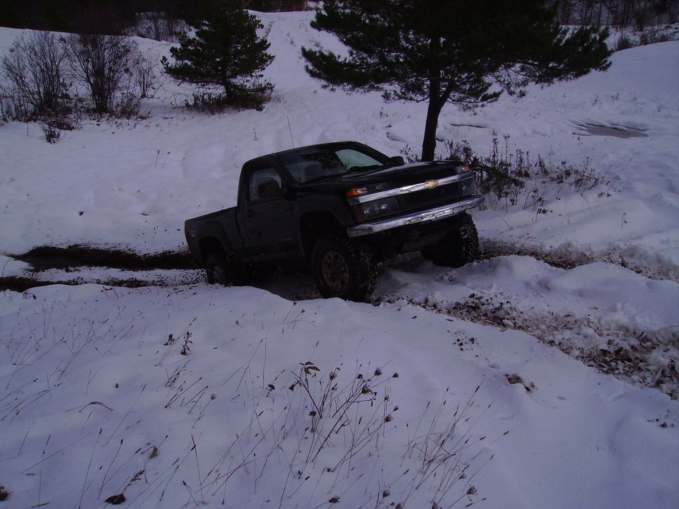 Black pickup truck with lifted suspension driving in snow, front 3/4 view