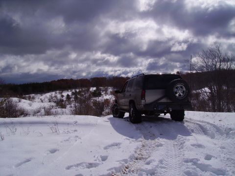 2000 Chevrolet Tahoe - An SUV navigates a snowy terrain under a cloudy sky, leaving tire tracks behind.
