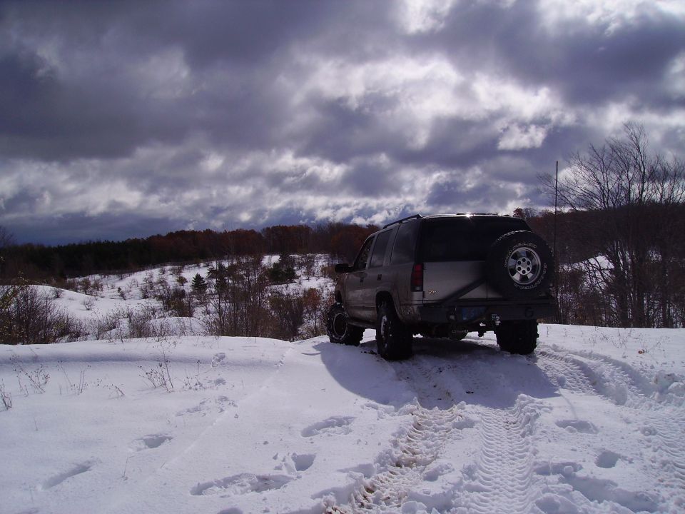 SUV with spare tire on back driving in snow, tire tracks visible