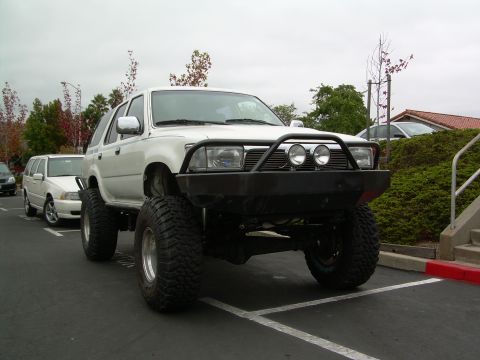 1993 Toyota 4Runner - Modified Toyota 4Runner with custom bumper and oversized tires parked in a lot.