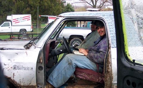 1978 Ford Bronco - Two men are inside the cab of a weathered pickup truck, with another truck visible in the background.