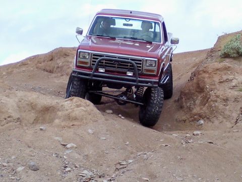 1991 Ford Bronco - This red pickup truck is navigating a steep, rocky incline on a dirt trail.