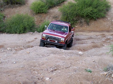 1991 Ford Bronco - A red pickup truck navigates a rough, dirt terrain.
