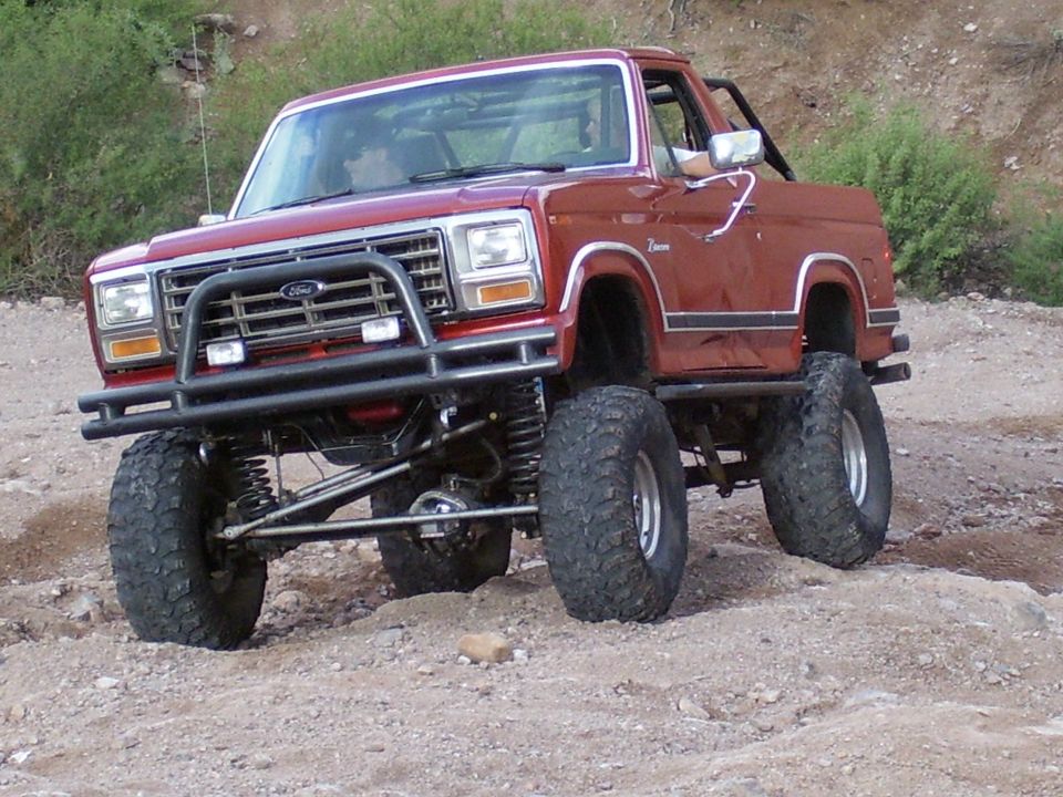 Red lifted Ford Bronco with off-road tires and brush guard driving on dirt