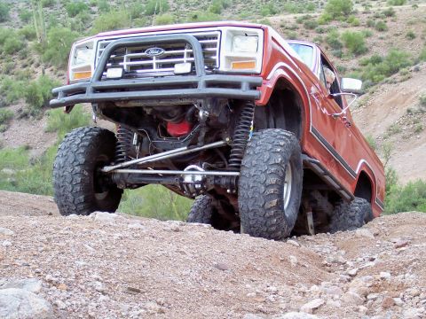 1991 Ford Bronco - This lifted Ford truck navigates a rocky, desert terrain with significant suspension articulation.