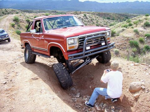 1991 Ford Bronco - A red Ford Bronco with a lifted suspension is captured off-roading while a person takes a photo of the vehicle.