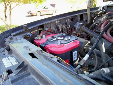 1991 Ford Bronco - Dual batteries installed in the engine bay of a vehicle, with another car in the background.