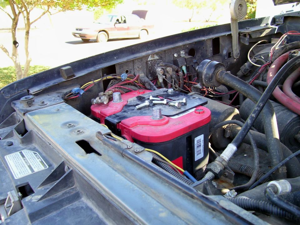 Engine bay showing dual red-top batteries and wiring; another car is visible in the background