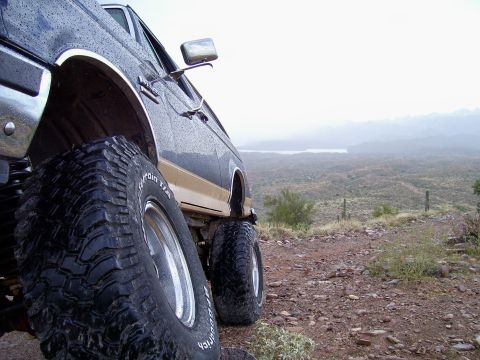 1991 Ford Bronco - A lifted Ford Bronco with aggressive tires sits on a dusty trail overlooking a vast, hazy landscape.