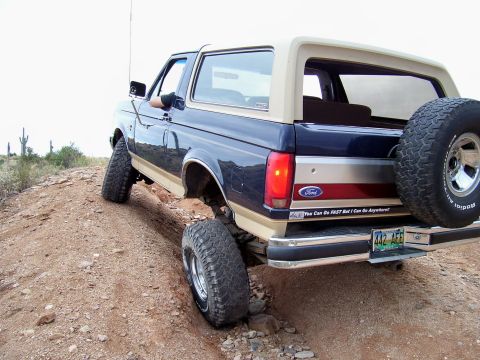 1991 Ford Bronco - This 1991 Ford Bronco is captured in a rear 3/4 view as it navigates a challenging dirt path, off-road terrain.