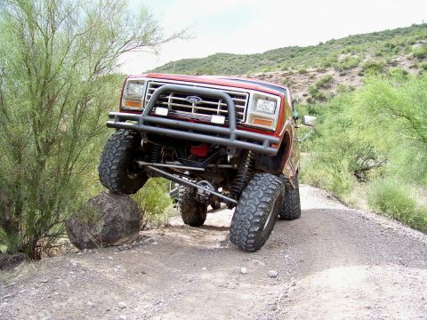 1991 Ford Bronco - This modified Ford Bronco is shown off-roading on a dirt path with a large rock.