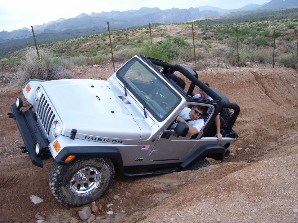Silver Jeep Wrangler Rubicon driving on a dirt trail with two people inside. Mountains in background
