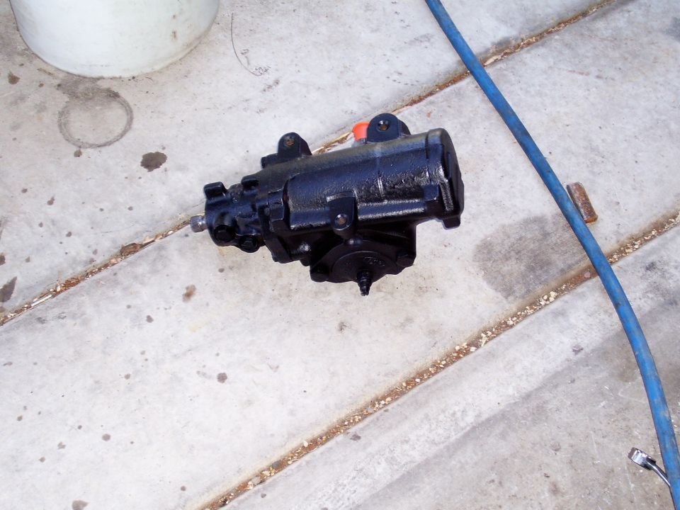 black steering gear box on concrete, blue hose nearby