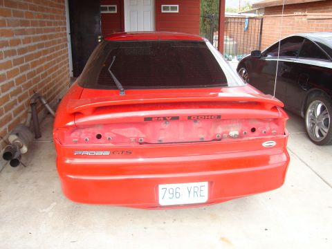 1997 Ford Probe - The rear of a red car is shown, with a black car parked to its right. The red car has a license plate and some visible badging.