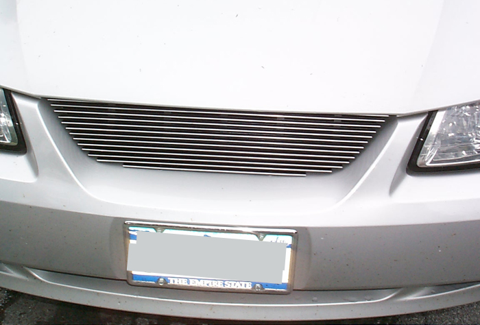 Silver car front with horizontal chrome grille and license plate frame reading "THE EMPIRE STATE"