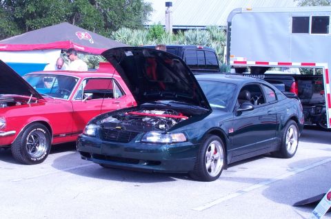 2006 Ford Mustang - A dark green coupe, possibly a GT model, is parked with its hood open at an outdoor event.