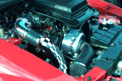 2006 Ford Mustang - The engine bay of a red 2006 Ford Mustang shows a Cobra supercharger and custom intake system.
