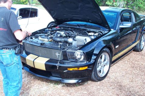 2006 Ford Mustang - Black 2006 Ford Mustang GT with hood open, gold stripes, and a white car in the background.