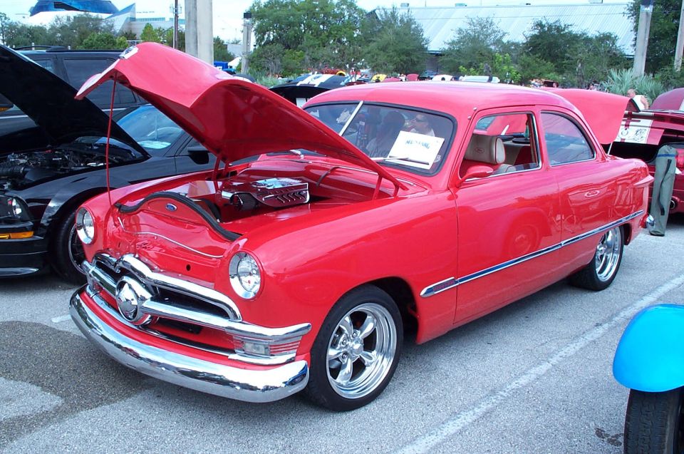 Red 1949 Ford Coupe with hood open, chrome grille, and custom wheels